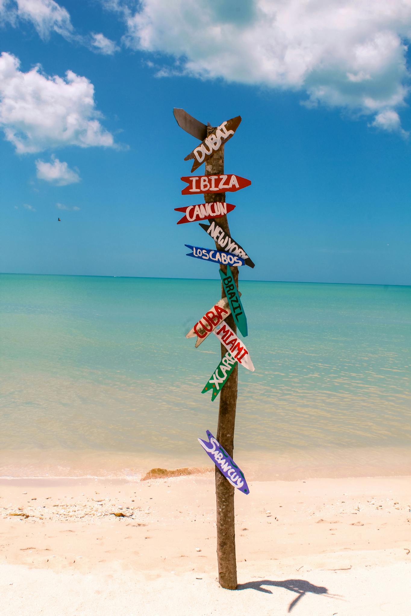 Vibrant directional signpost on a sunny Sabancuy beach, Mexico, with clear sea and sky.